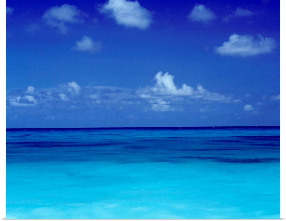 Big square photo art of a clear ocean with puffy clouds in a blue sky.