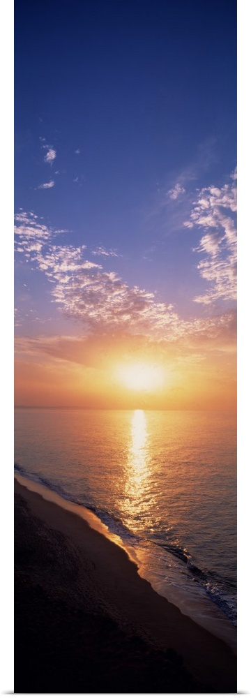 Vertical panorama of the sun rising on the horizon of the Atlantic ocean, as seen from a sandy beach in Western Europe.