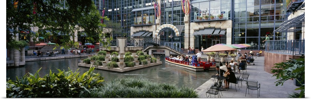 Oversized photograph on a horizontal canvas of the Rivercenter mall in San Antonio, Texas.  A small boat floats through th...