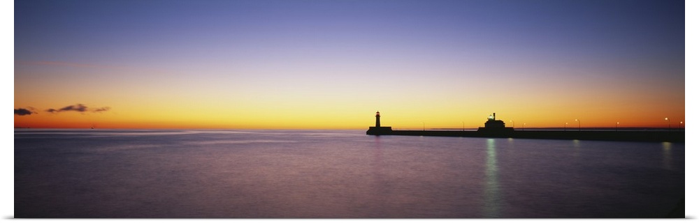 Panoramic photo on canvas of a lighthouse and pier silhouetted against a sunset.