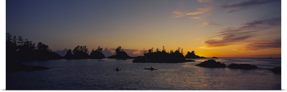 Tiny islands and boats on the water are silhouetted by the sunset that has gone below the horizon.