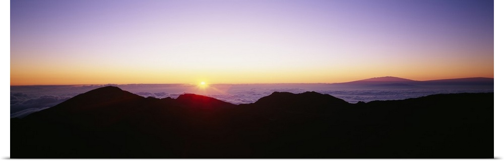 The sun begins to rise above the horizon and silhouettes a mountain range in the foreground of the picture.