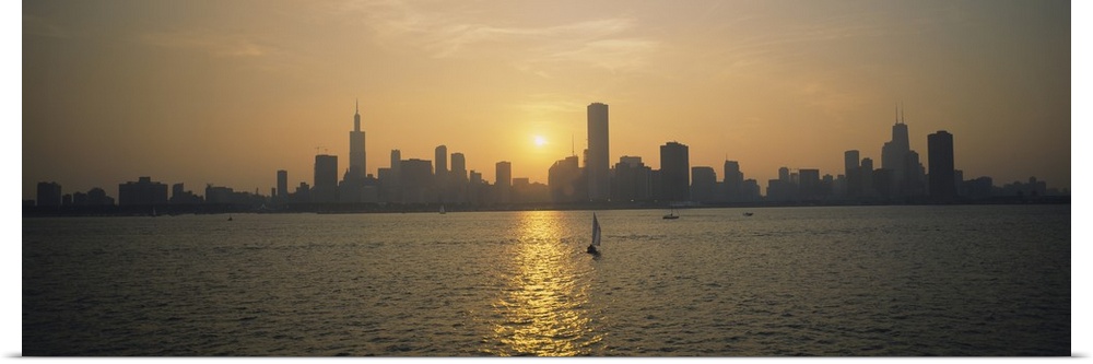 Wide angle photograph of a distant Chicago skyline, silhouetted by the setting sun, several small boats float on the water...