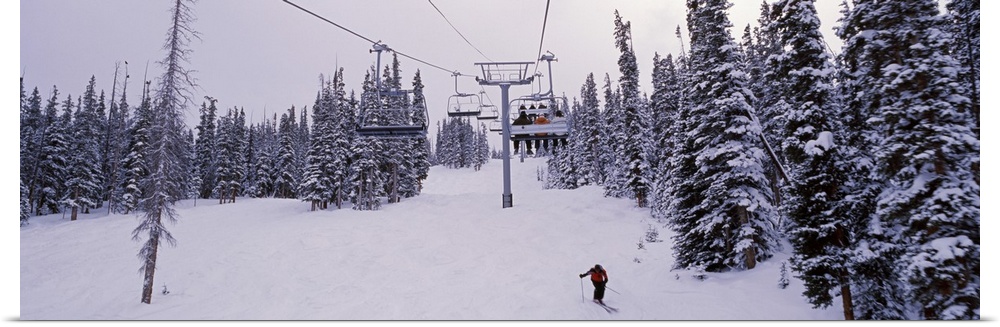 Panoramic photograph on a giant canvas of a ski lift surrounded by snow covered trees, one skier on the ground, at the Key...