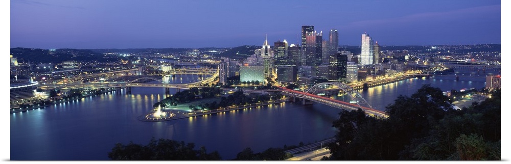 Large panoramic photo of downtown Pittsburgh, Pennsylvania (PA) lit up at night. Multiple bridges visible.