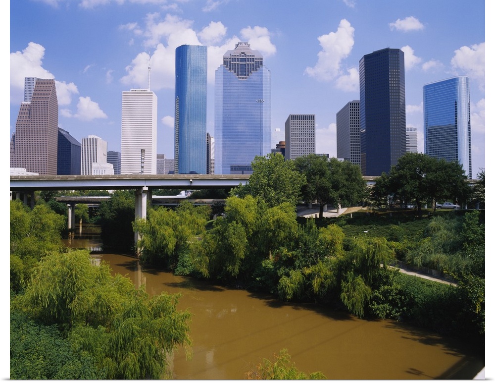 This is a nearly square landscape photograph of cityos downtown skyscrapers and a river that passes through a park and und...