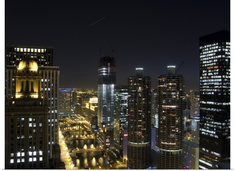 Tall buildings in Chicago are illuminated under a night sky that has a single shooting star photographed.