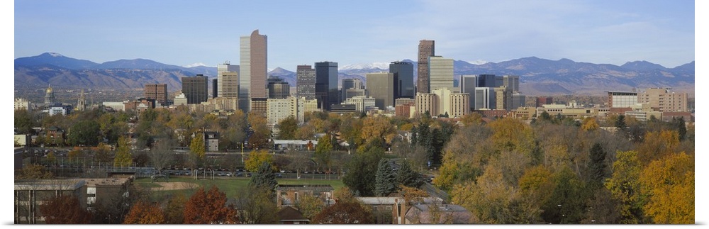 An urban city skyline nestled in a Rocky Mountain valley with a baseball field and several trees along the edge.