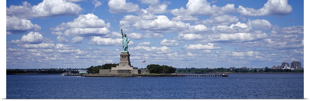A panorama of the Statue of Liberty and the NY Harbor with a blue sky in background.