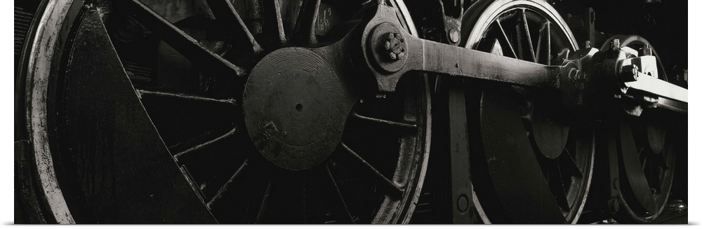 Panoramic photograph displays a monochromatic close-up looking at the components of a train that are attached to the rails.