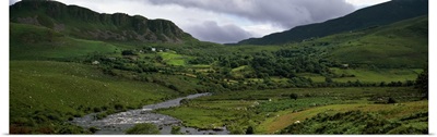 Stream through lush mountain landscape, distant cottages, Ireland
