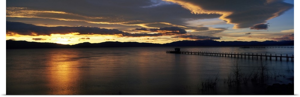 Panoramic photograph of pier stretching into water at dawn.  The sky is dark and cloudy.