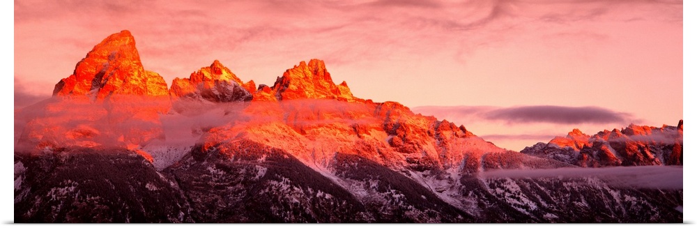 The sun rises on rugged mountains casting a warm hue of sunlight over the tops of them with darkness at the bottom.