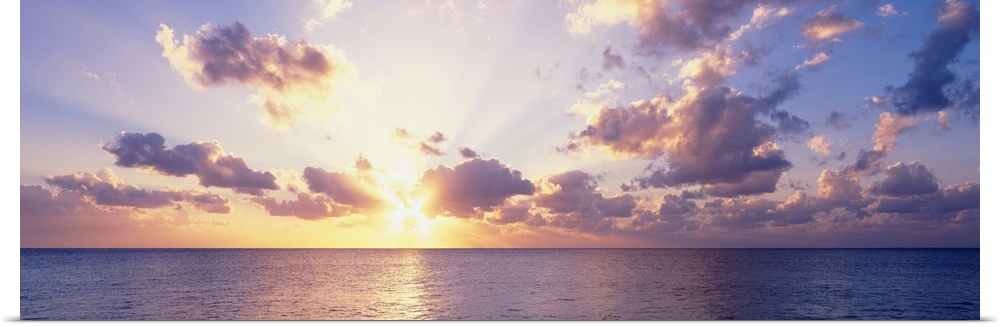 Panoramic photograph showcases the sun beginning to set and glisten over the waters within the Caribbean Sea.