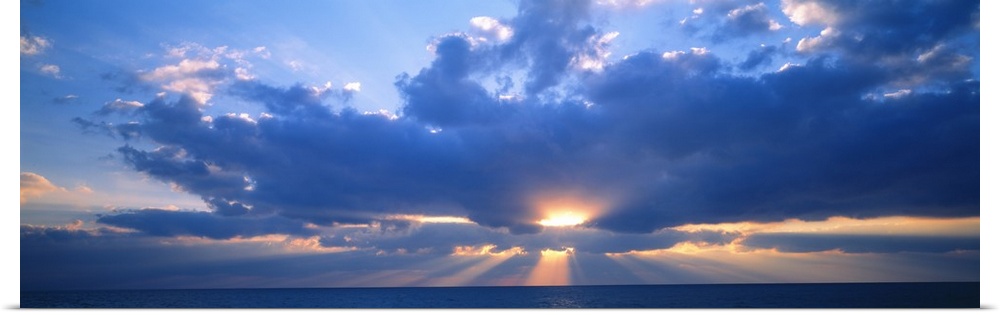 Panoramic photograph of the sun peaking through large, fluffy clouds as it sets over the Gulf of Mexico in Florida.