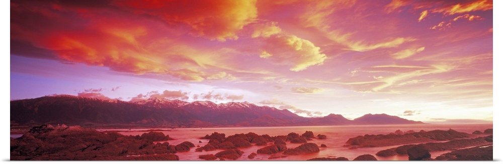 The sunset paints the sky with warm tones that hang over a mountain range and a body of water.