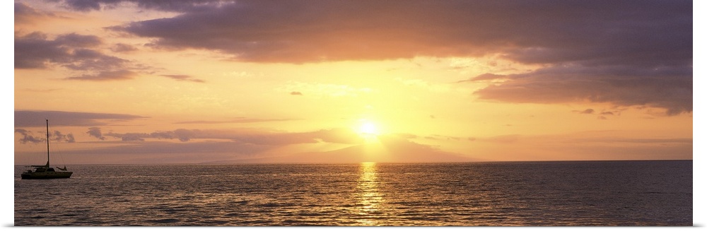 Panoramic photograph on a large wall hanging of a single boat floating on rippling waters at sunset, in Maui, Hawaii.