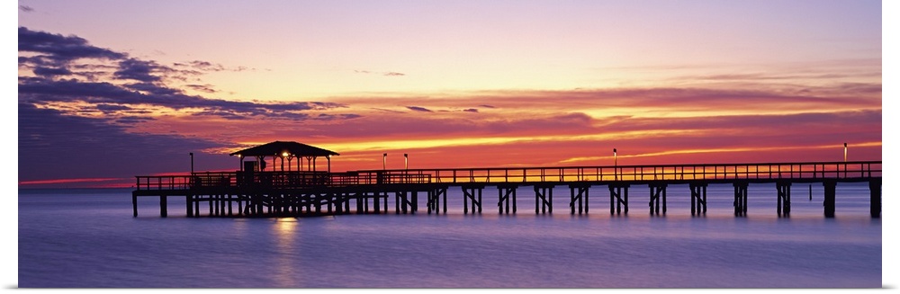Wide angle photograph of Mobile Pier surrounded by deep purple waters beneath a vibrant sunset, in Mobile, Alabama.