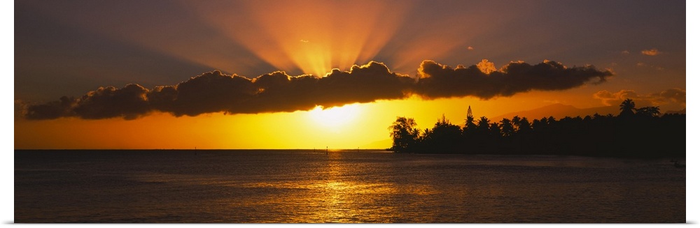 Panoramic photograph of the sun setting behind the clouds over the water in Tahiti.