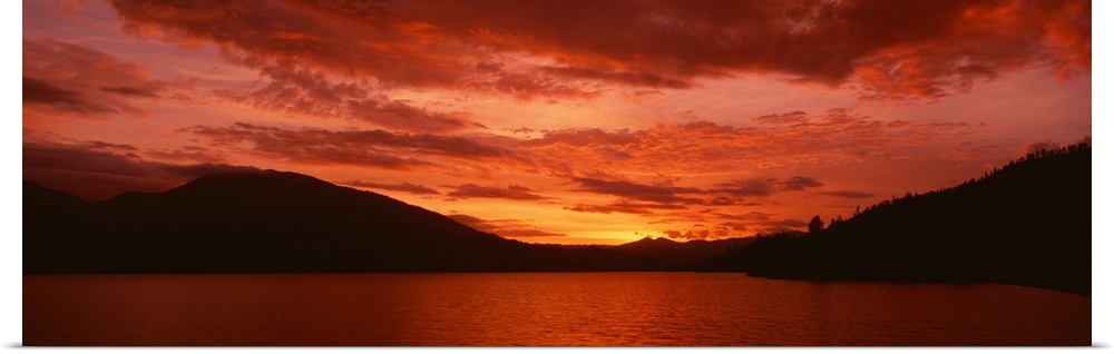 Panoramic photograph of a vibrant fiery sunset over a silhouetted mountain landscape and Whiskeytown Lake in California.
