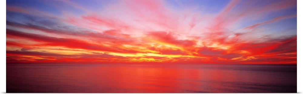 Wide angle photograph on a giant wall hanging of the sky full of streaking clouds during a vibrant sunset over the Pacific...