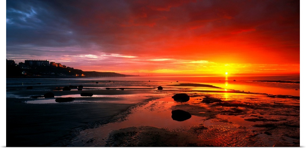 Panoramic photograph that captures a colorful sunset on the shores of England.  The calm beach is highly contrasted by the...