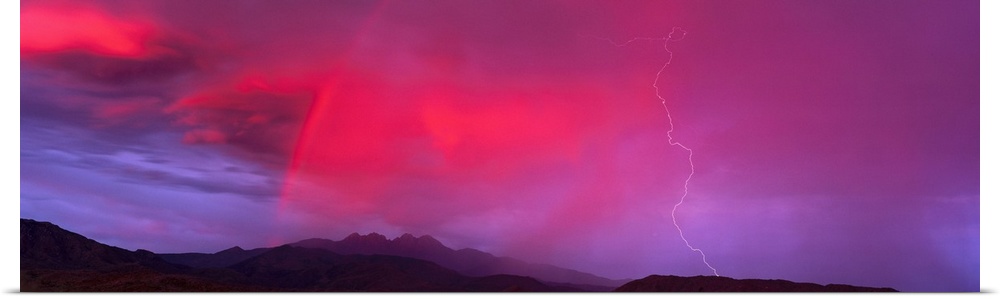 This panoramic photograph is taken of a sunset sky that is highlighted with hot pink and a bolt of lightning is striking d...