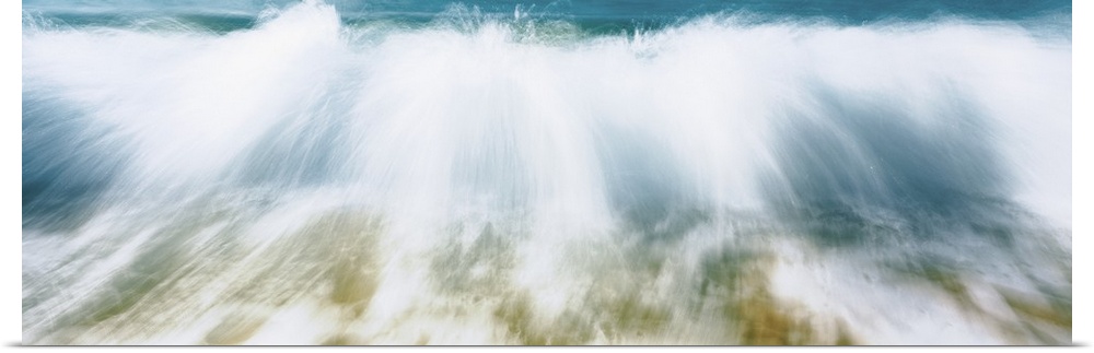 Up-close panoramic photograph of wave crashing onto beach creating spray.