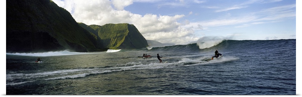 This is a panoramic photograph of ocean swells and volcanic cliffs and surfers waiting to catch the next wave.