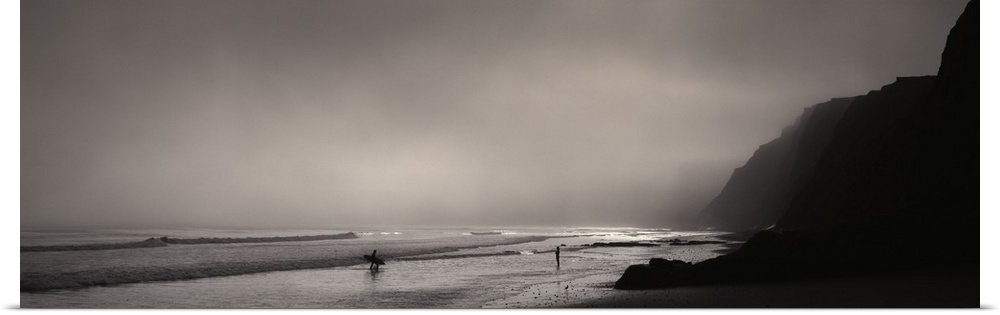 Panoramic photograph on a giant canvas of a dark, foggy sky over Point Reyes National Seashore, where two surfers walk awa...