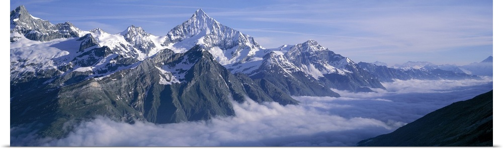 Panoramic, aerial photograph of thick clouds surrounding the snow capped Swiss Alps, against a blue sky, in Switzerland.