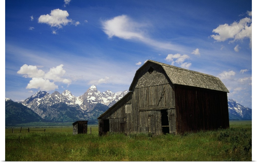 Large photograph of a rustic barn in a grassy field with a mountain range behind it in Grand Teton National Park, Wyoming.