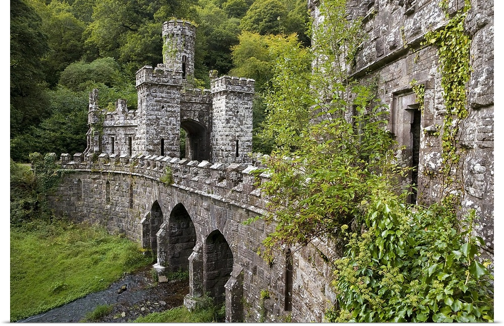 A side angle view of a large stone bridge and towers that are surrounded by greenery in Ireland.
