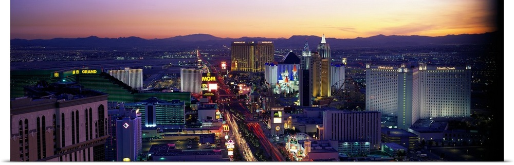Panoramic photograph of ""Sin City"" skyline at sunset with buildings lit up and mountains in the distance.