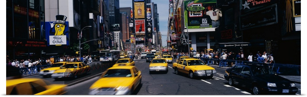 Wide angle photograph of many taxi cabs rushing through the streets, surrounded by the large advertising signs of Times Sq...