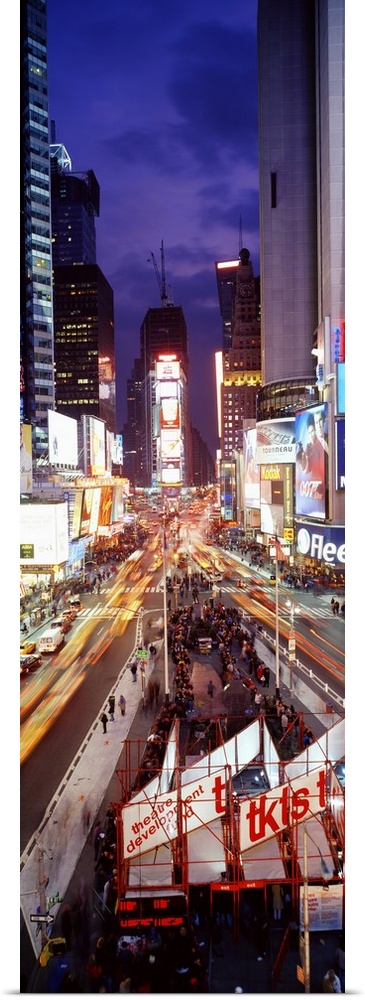 Vertical panoramic of a busy Times Square at night with traffic lined streets and tourists in line to buy theatre tickets.