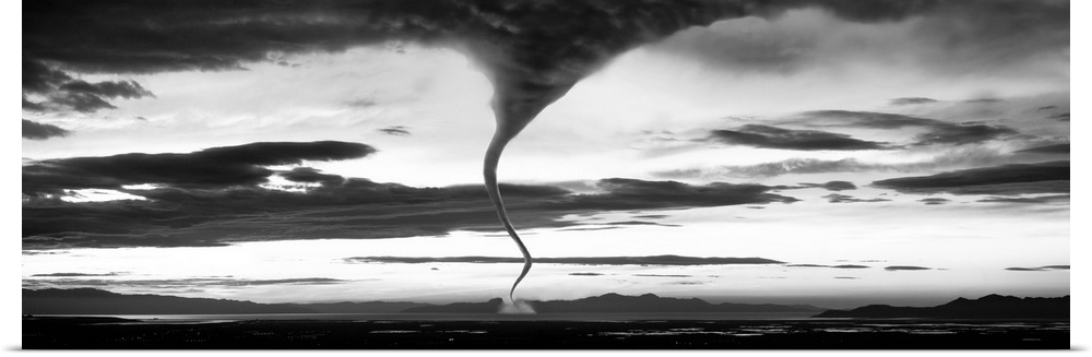 Panoramic photograph of funnel cloud reaching down to earth surrounded by a dark, cloudy, stormy sky.