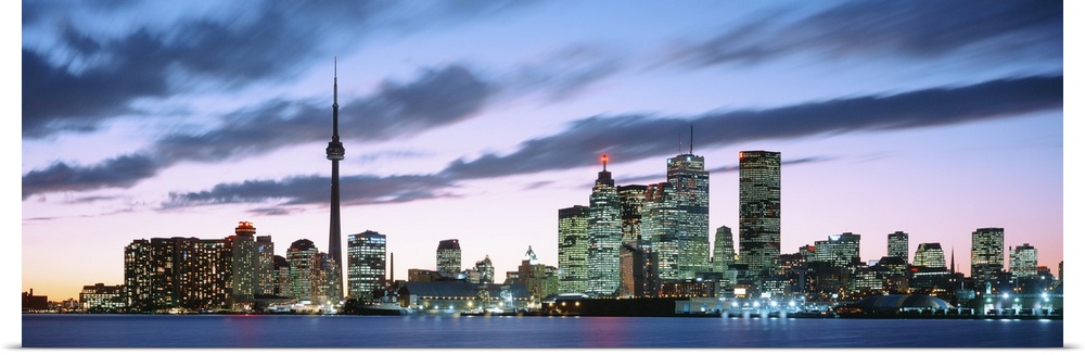 Panoramic photograph of the modern city of Toronto at twilight, under dark clouds in a pastel sky lit up by the sunset.