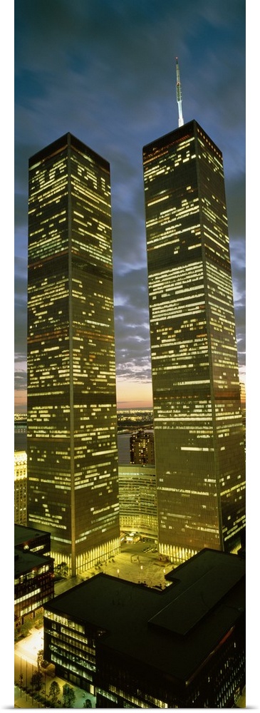 Panoramic photograph focuses on the nicknamed ""Twin Towers"" lit up at nighttime.  At the base of the skyscrapers, the su...