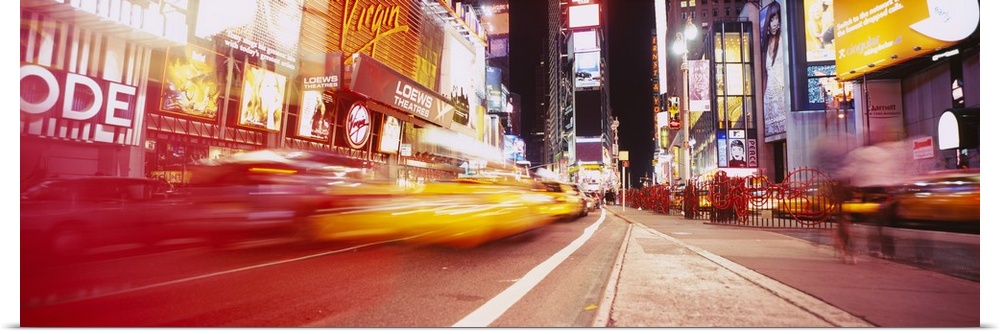 Big, horizontal photograph of blurred traffic driving down the road leading through Times Square, at night in New York City.