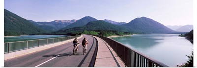 Two cyclists moving on a bridge across a lake, Sylvenstein Lake, Bavaria, Germany