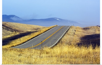 Two lane highway through autumn color grasses, distant mountains in mist, Montana