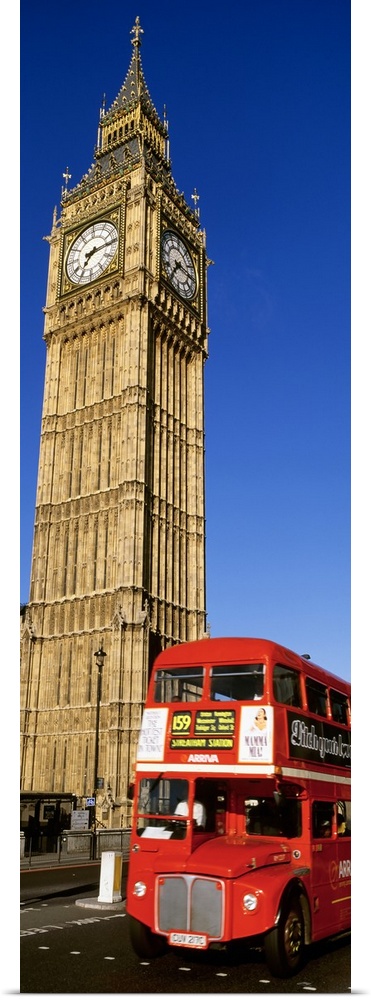 Vertical shot of Big Ben and a red London city bus driving by.