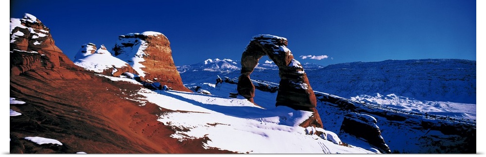 Snow covers desert land and stone arches that are photographed in panoramic view.
