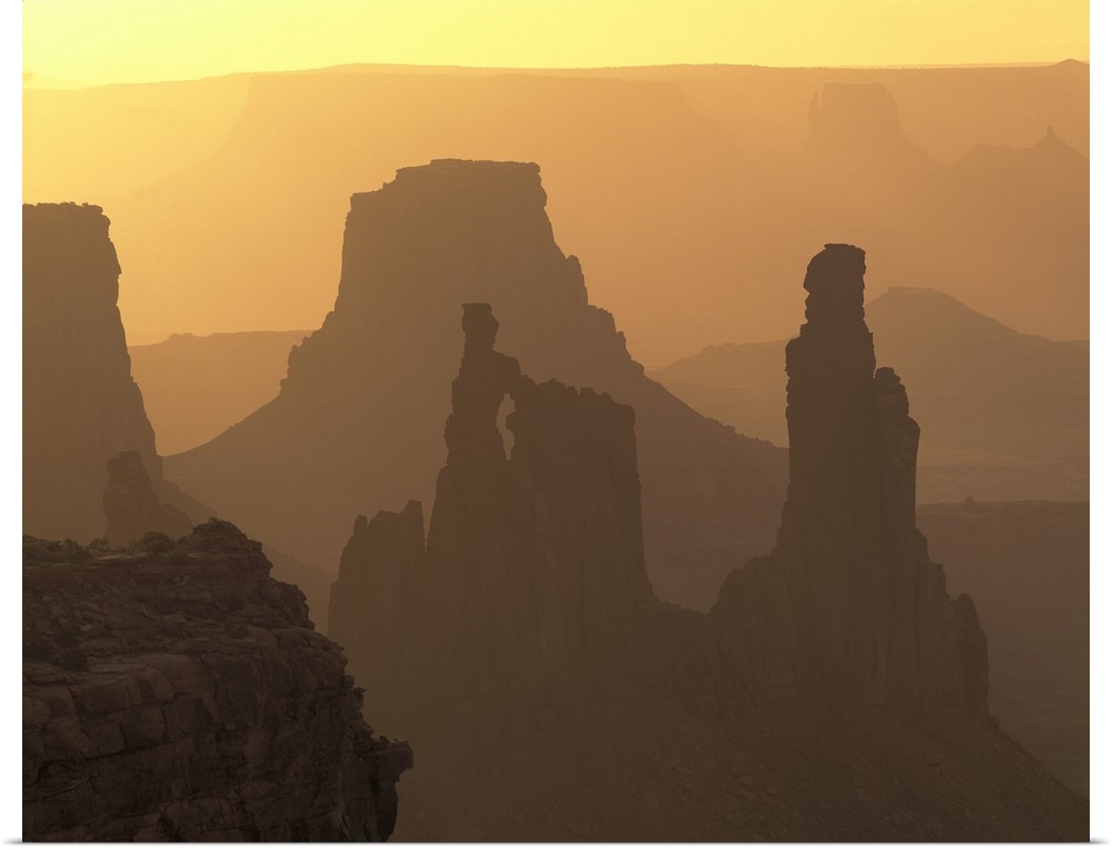 The large rock formations in Canyonlands National Park is silhouetted by the sunset that is out of view.