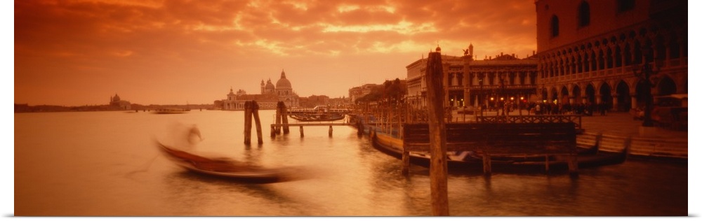 Panorama of a small Italian harbor with a blurred gondola coming into port at sunset.
