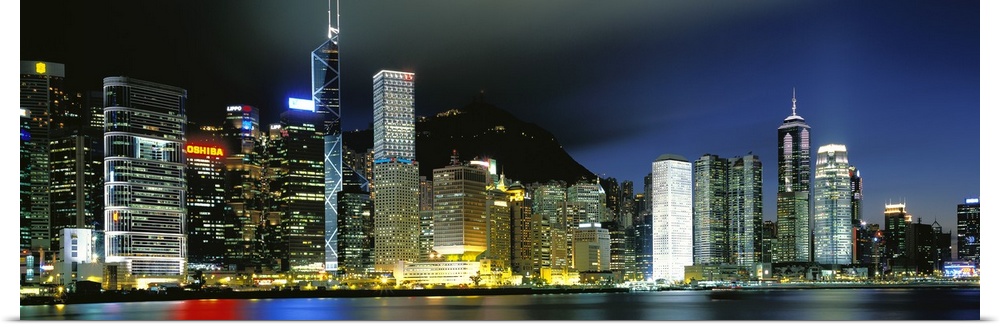 Panoramic photograph of city skyline.  The buildings are lit up in the night sky and are reflected in the waterfront.