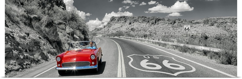Panoramic photograph displays a classic car cruising down a highway with rocky canyons on both sides of the road.  The col...