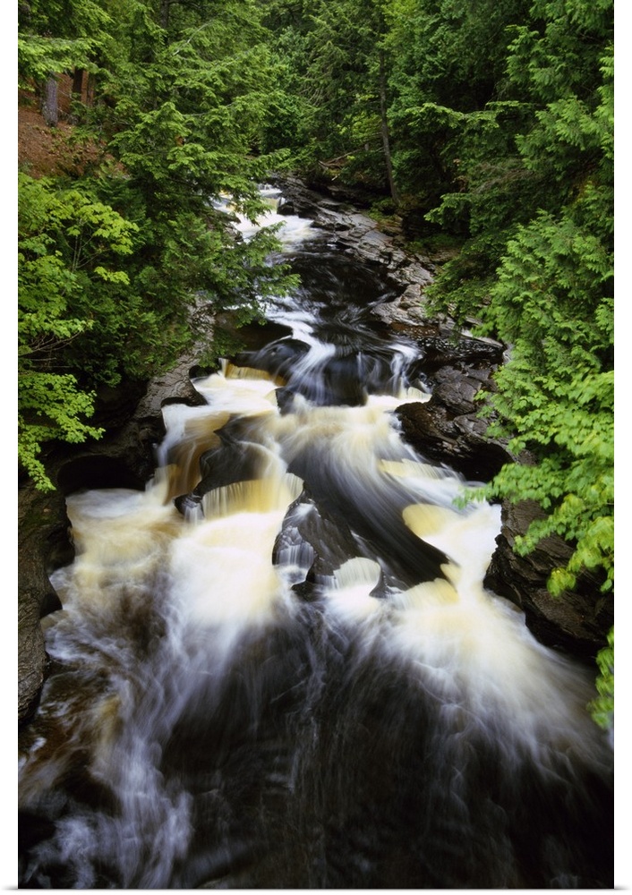 Giant, vertical, high angle photograph of water rushing through the rocky Presque Isle River, surrounded by green trees at...