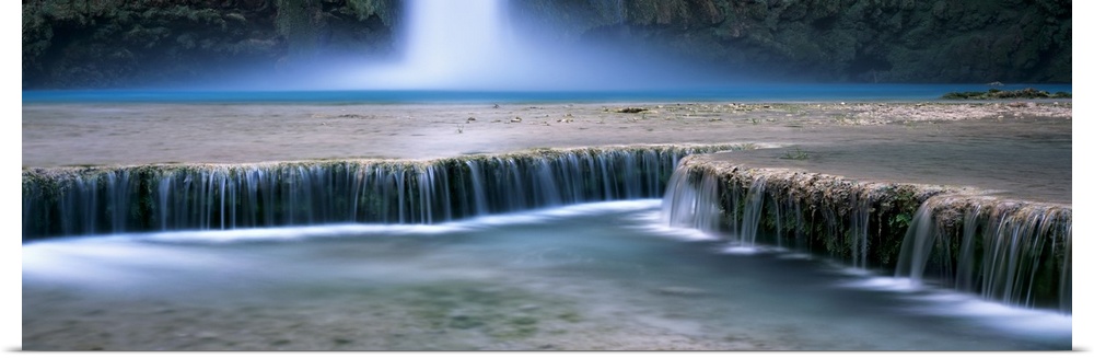 This is a panoramic, time lapsed photograph of water flowing over shallow waterfalls in a desert oasis.